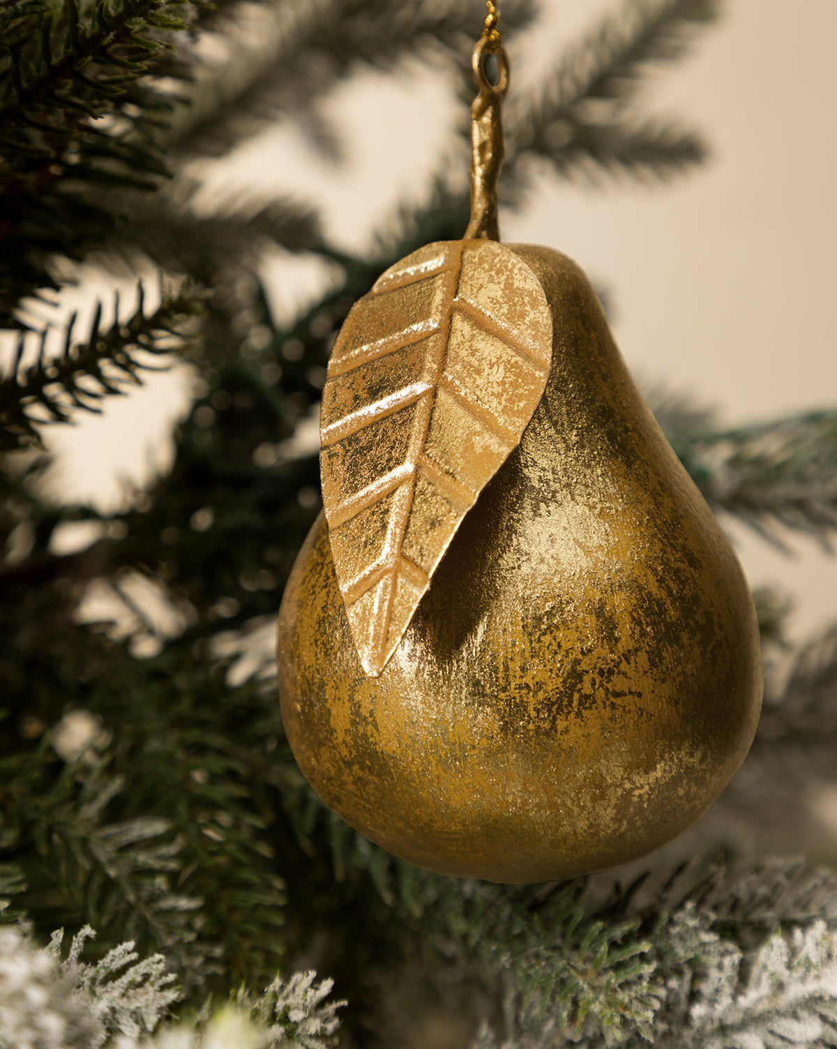 The Gilded Pear Ornament, featuring a metallic leaf, hangs on a green Christmas tree branch and brings vintage holiday charm, by Vendixs