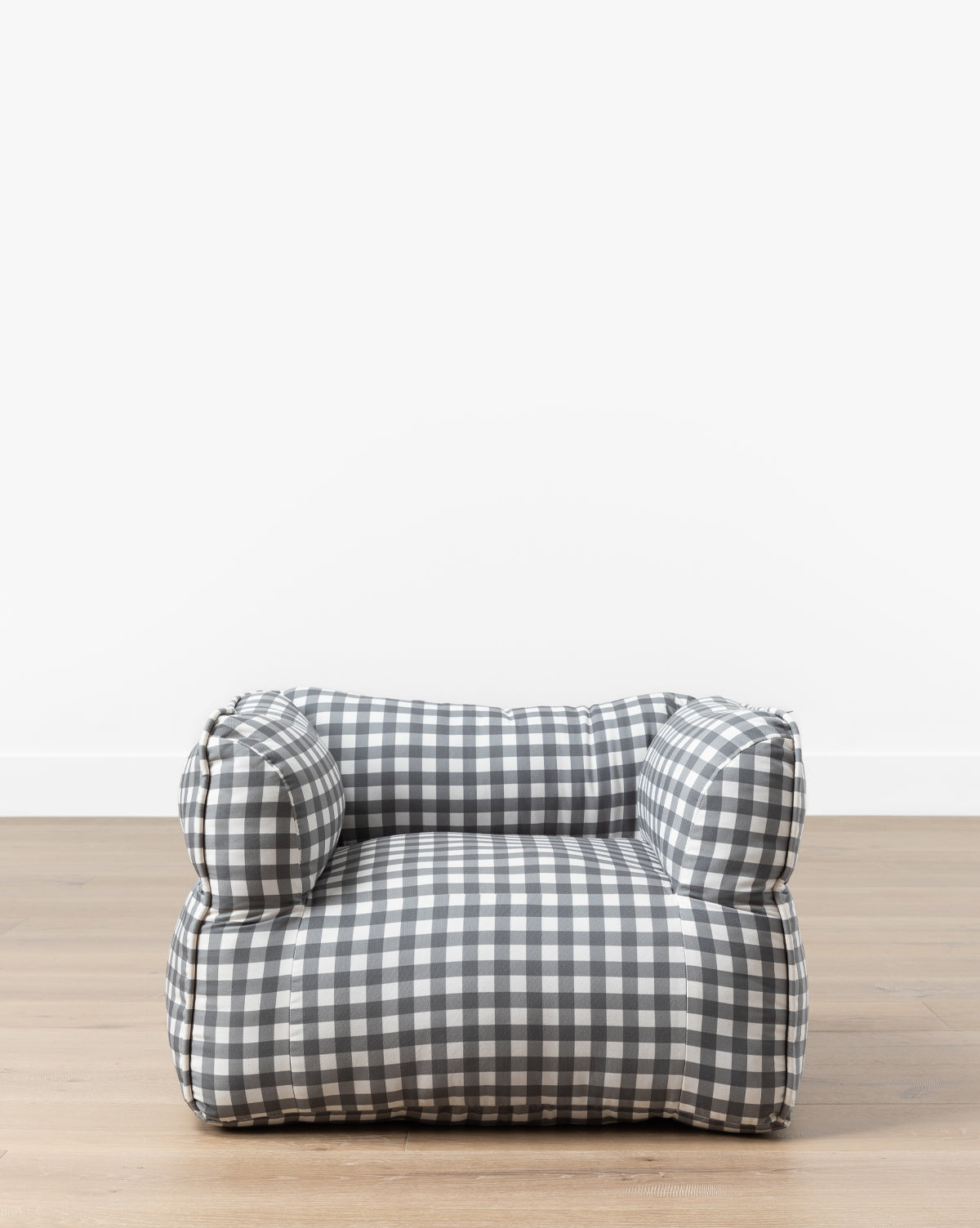 The Gingham Kids Chair features a low, plush design with black and white gingham fabric, sitting on a light wooden floor against a plain white wall—ideal for any childs room, by Vendixs