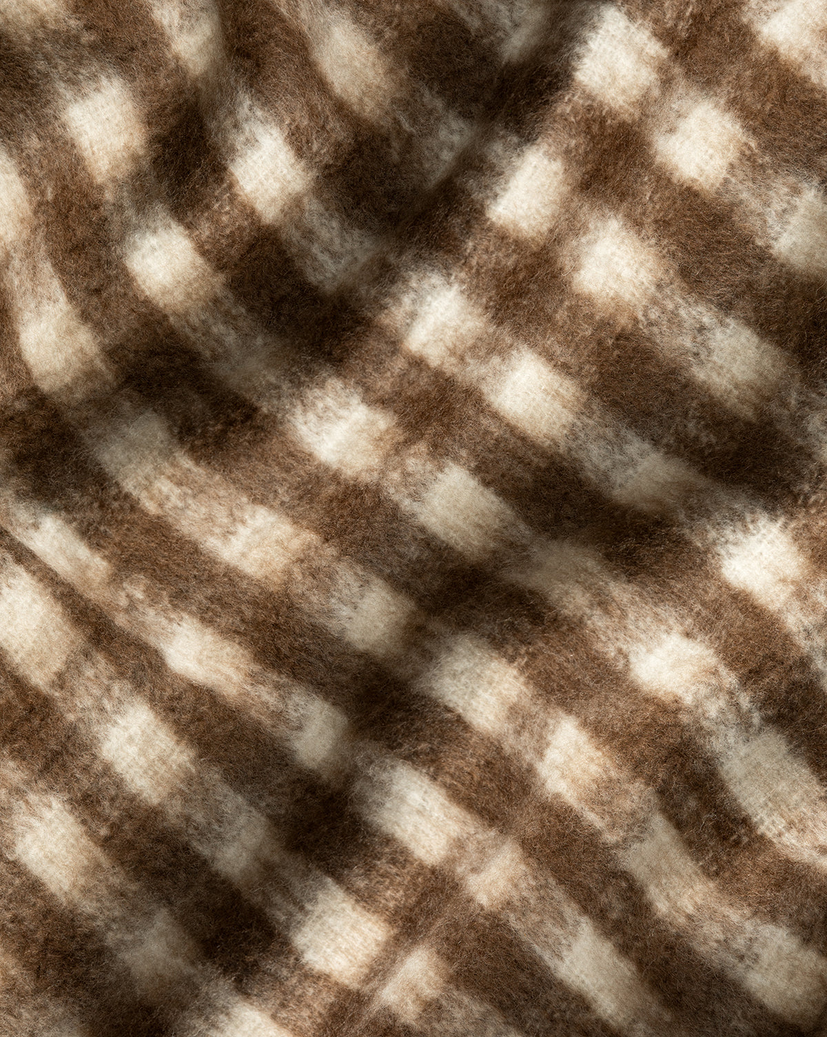 A close-up of the Indaba Gingham Wool Blend Throw, showcasing its soft, fuzzy texture and brown and cream checkered pattern with gentle folds for a cozy feel. Vendixs