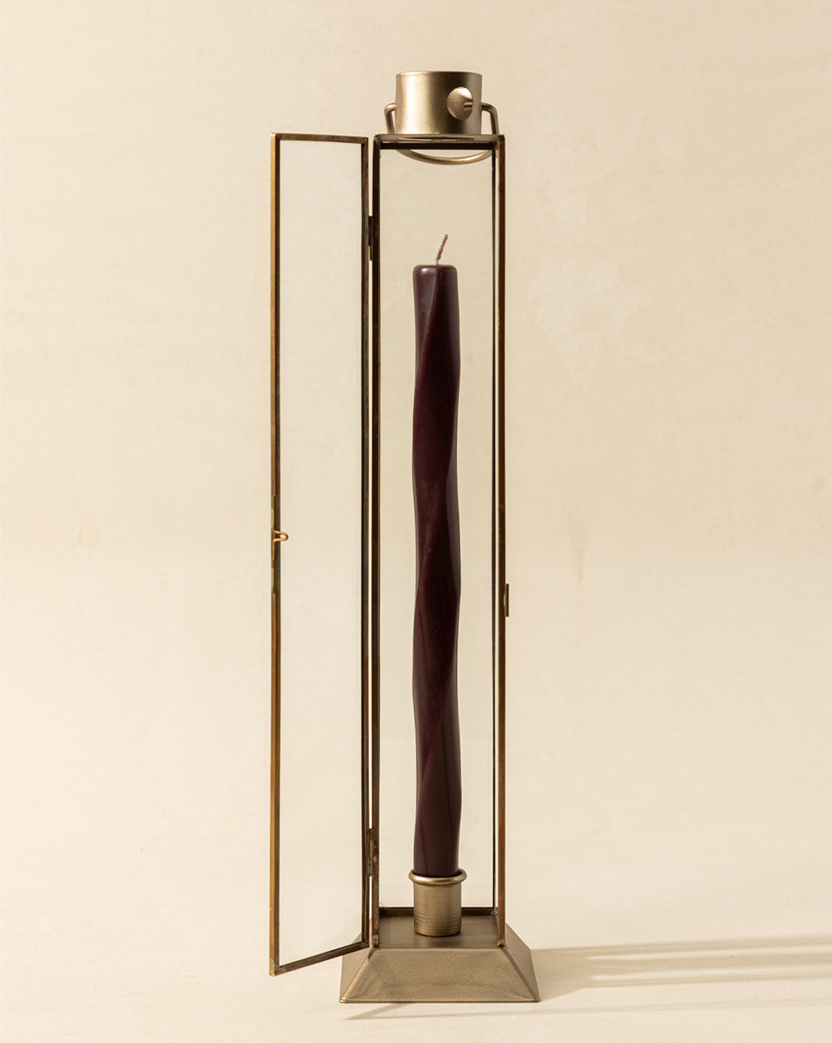 A tall, twisted dark burgundy candle is displayed in the Glass & Metal Lantern Taper Holder with one door open against a neutral background for an elegant, stylish presentation, by Vendixs