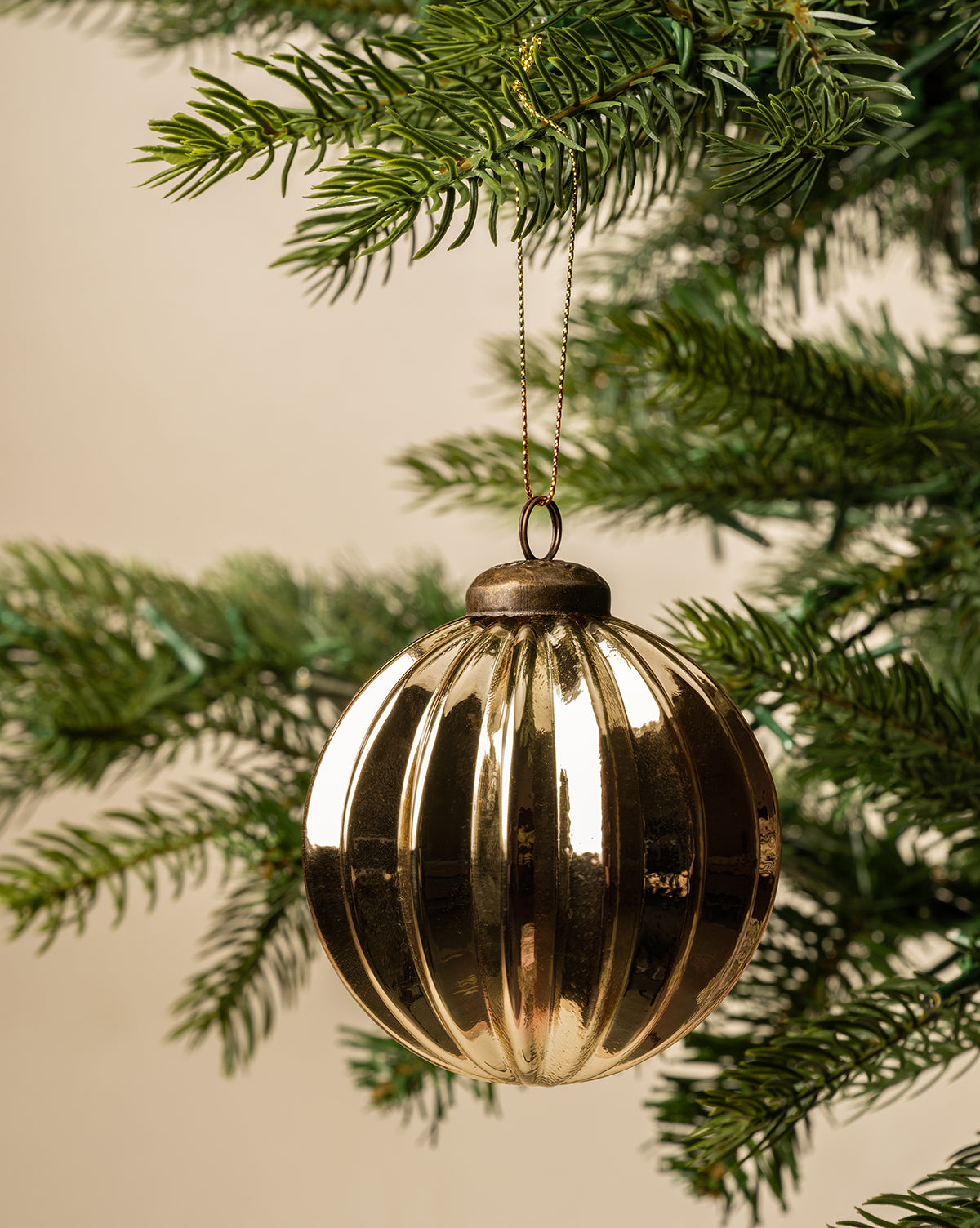 A 3" Gold Bauble with a shiny finish hangs from the branch of a green Christmas tree against a neutral background, by Vendixs