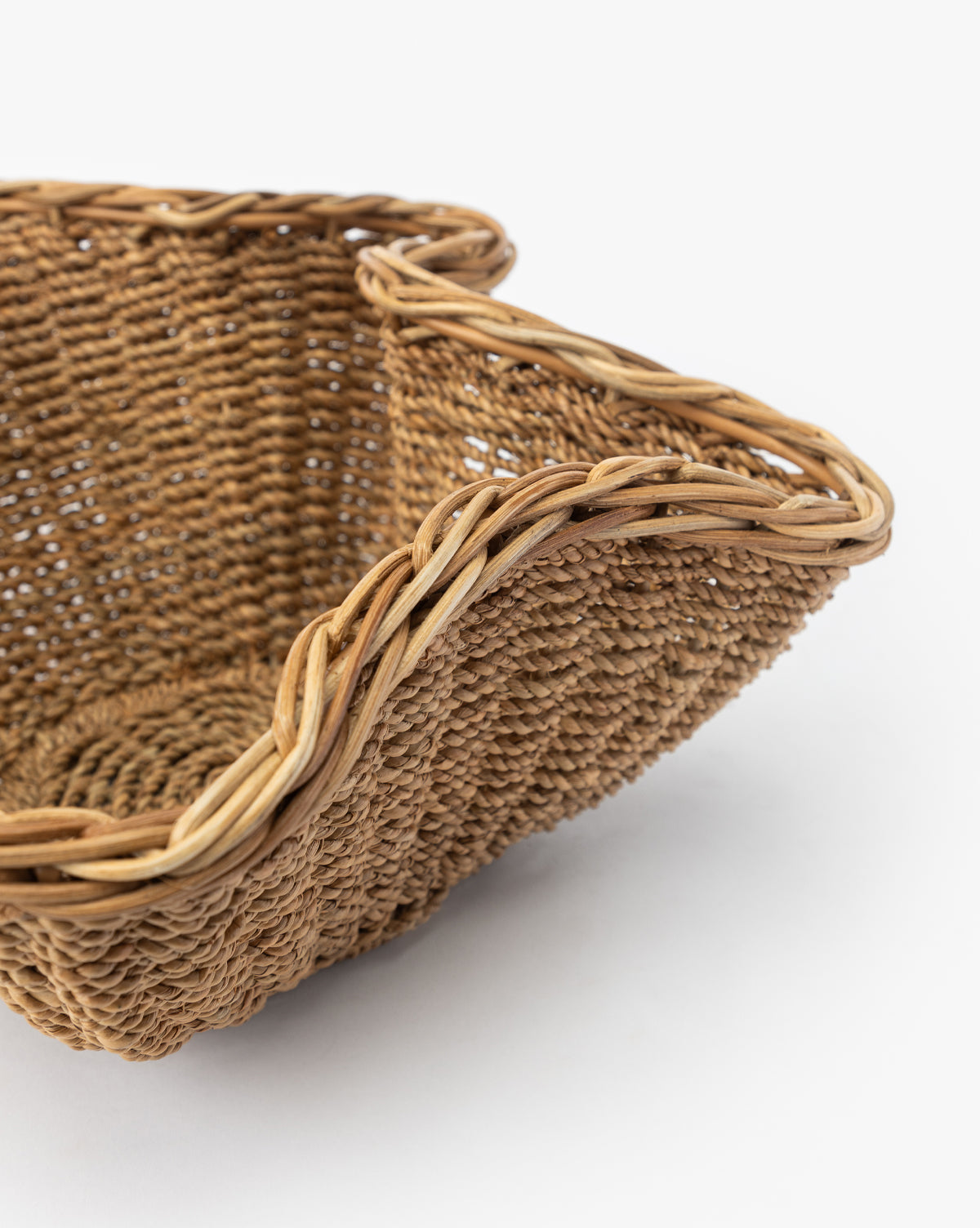 A close-up of the Goulding Woven Bowl—a square rattan basket with curved, braided edges—ideal as entryway decor or a stylish wicker bowl, shown against a plain white background, by Vendixs