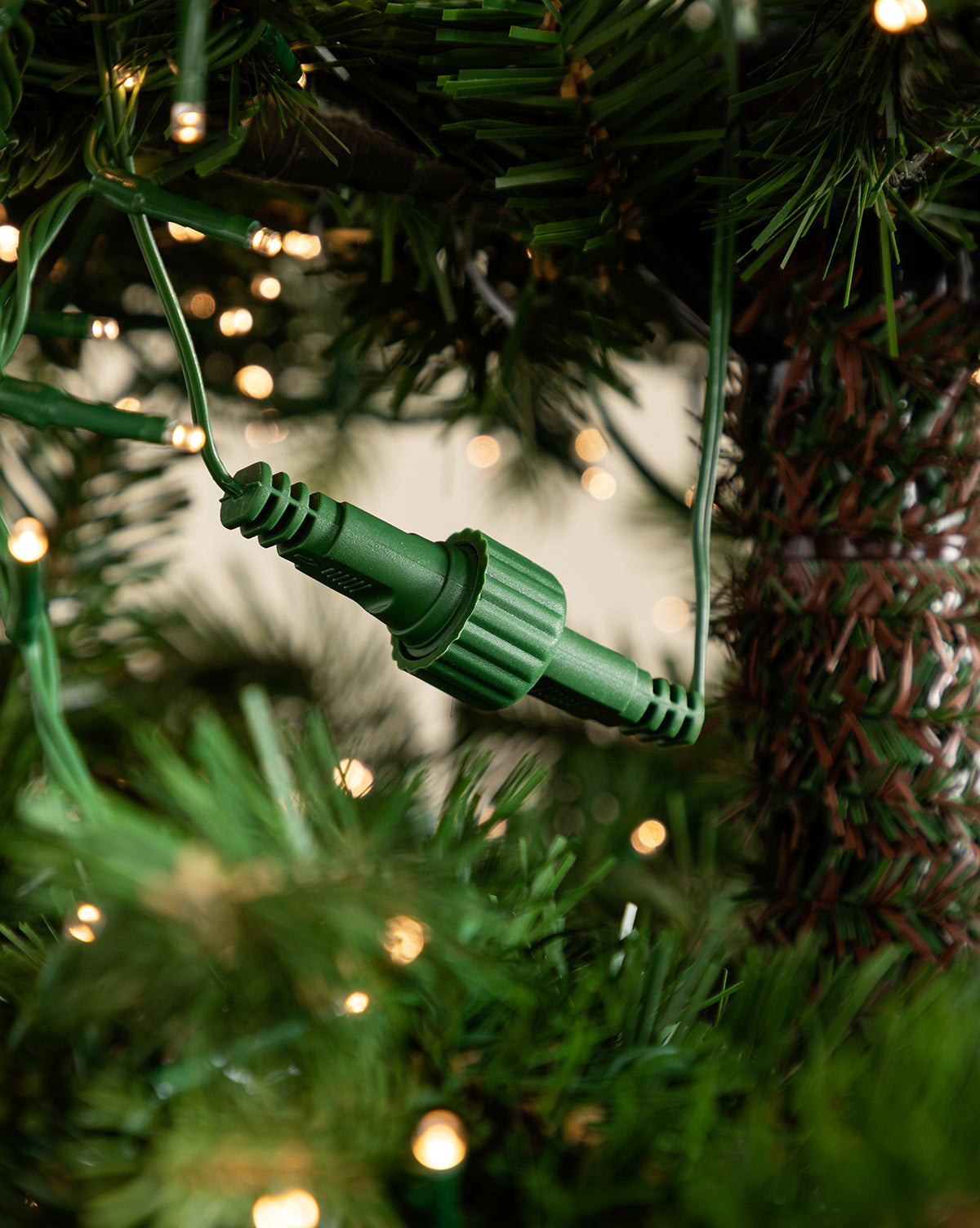 A green electrical connector nestled among branches of the 9' Grandis Fir Pre-Lit Faux Tree, surrounded by glowing string lights on this realistic artificial Christmas tree, by Vendixs