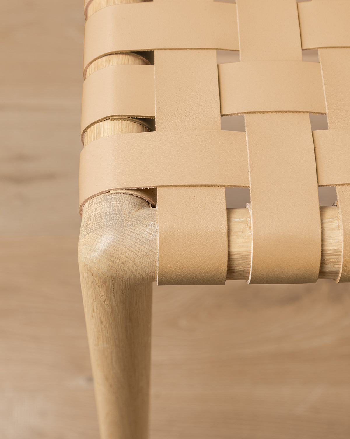 Close-up view of the Greely Stool, featuring a woven light tan aniline-dyed leather seat and a wooden leg, highlighting the interlacing pattern and smooth wood grain by Vendixs