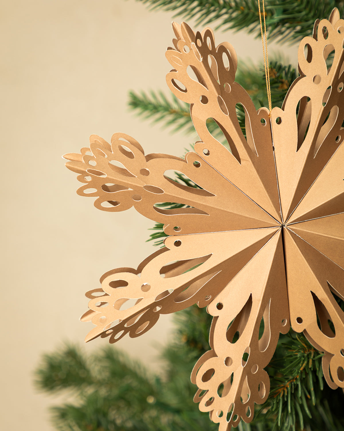A set of three Handmade Assorted Recycled Paper Snowflakes adds eco-friendly charm and neutral hues to your holiday decor, hanging beautifully on a green Christmas tree branch against a simple beige background, by Vendixs