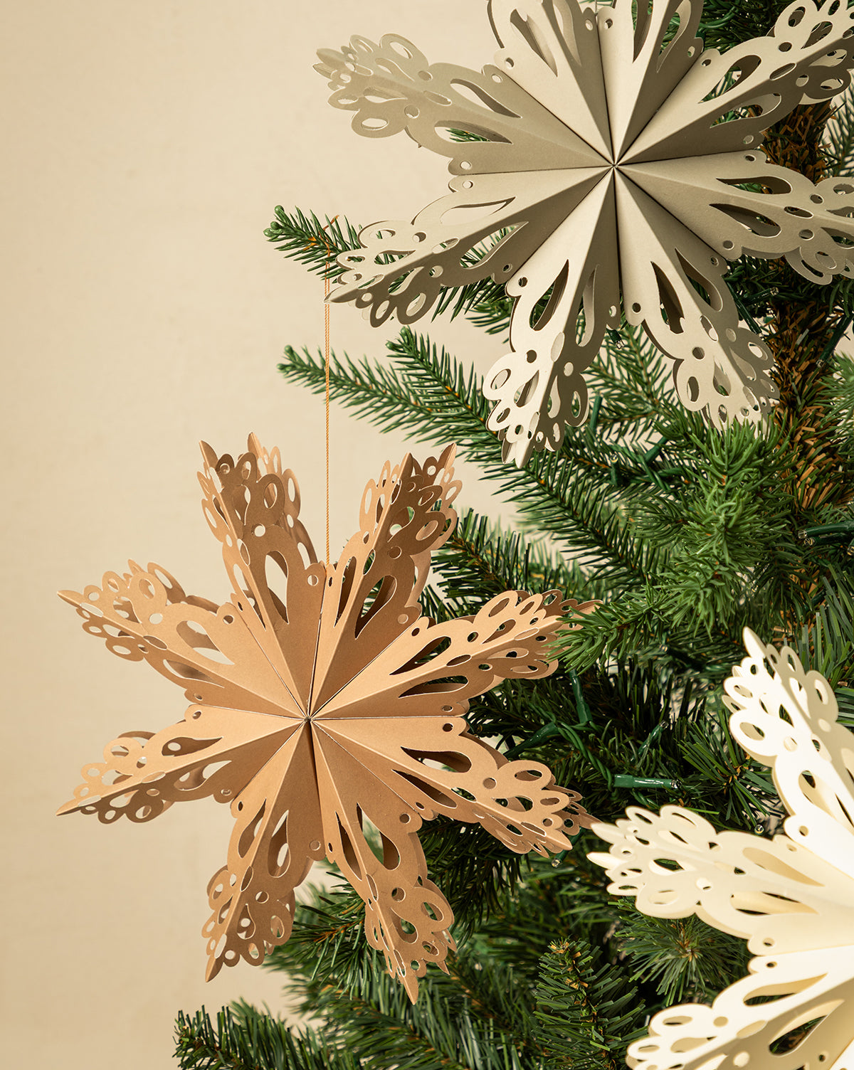 Handmade Assorted Recycled Paper Snowflakes (Set of 3) in neutral beige and cream hang from a green Christmas tree, adding eco-friendly style to your holiday décor against a light background, by Vendixs
