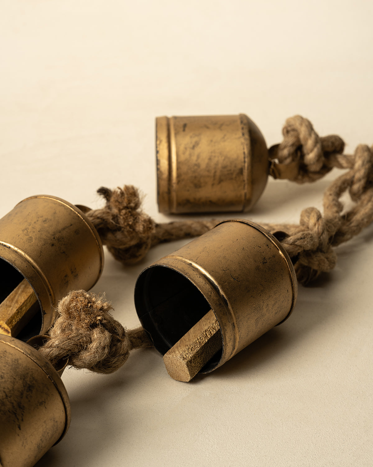 A close-up of three Hanging Iron Bells, featuring a weathered gold finish and wooden clappers, each strung on a thick coarse rope. Perfect for adding antique charm to your holiday décor, by Vendixs