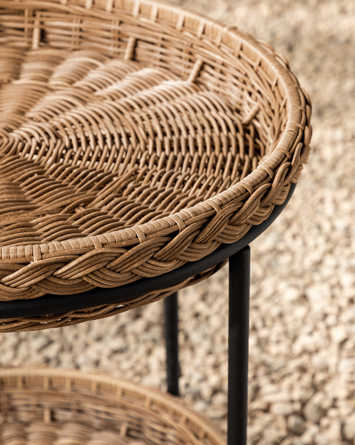 Close-up of the Haviland Bar Cart featuring weather-resistant round wicker with a braided edge, black metal legs, and a tightly woven surface—ideal for outdoor entertaining against a blurred gravel or pebble ground, by Vendixs