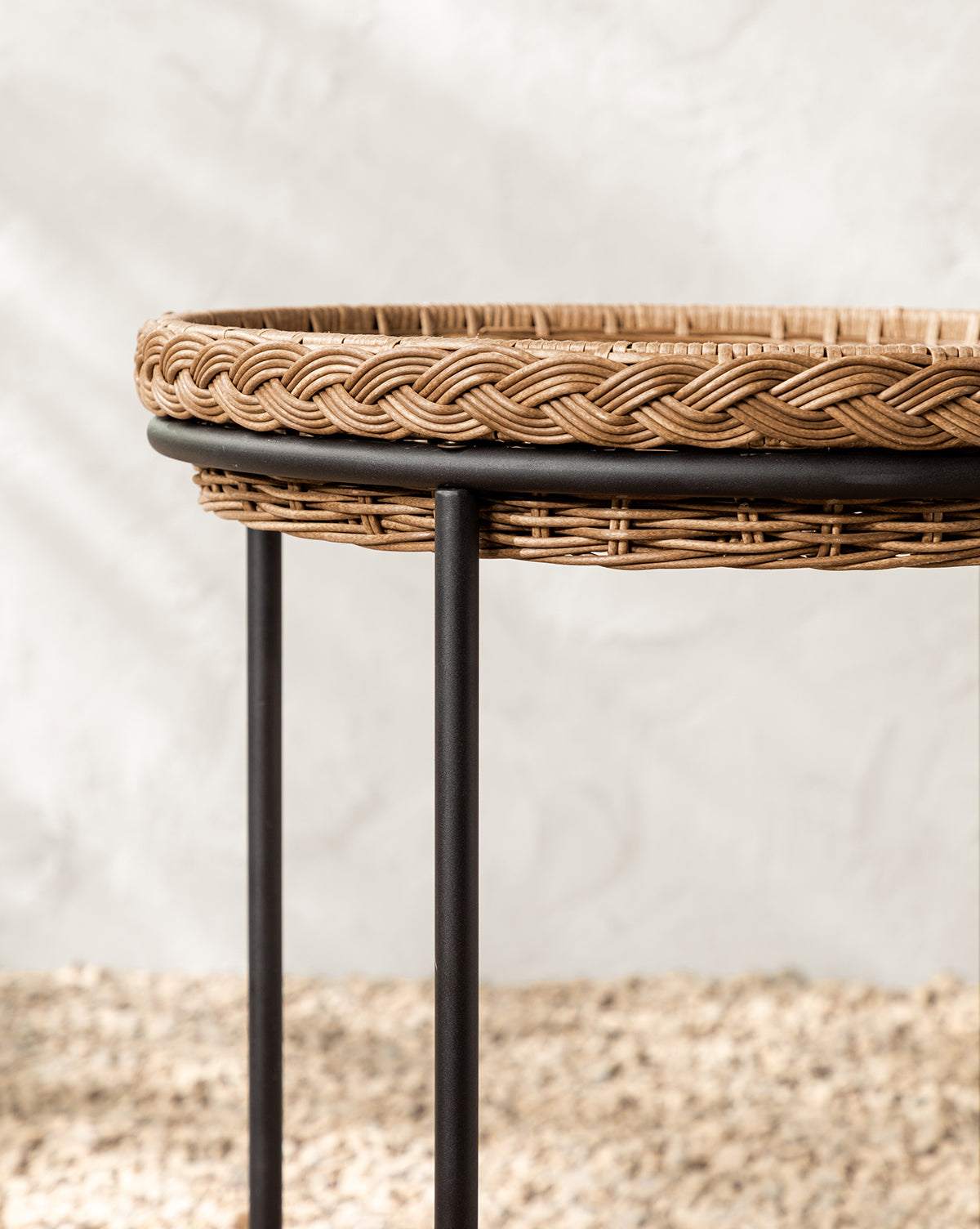 A close-up of the Haviland Bar Cart, featuring weather-resistant wicker with a braided rim and black metal legs, sits on a textured beige surface against a neutral backdrop—perfect for stylish outdoor entertaining, by Vendixs