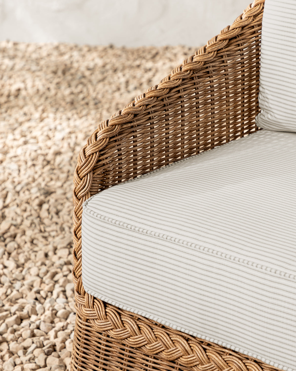 Close-up of the Haviland Outdoor Dining Chair with Perennials Taupe Stripe cushion, featuring weather-resistant wicker, braided edge detail, and woven texture, set on light-colored pebbles by McGee & Co.