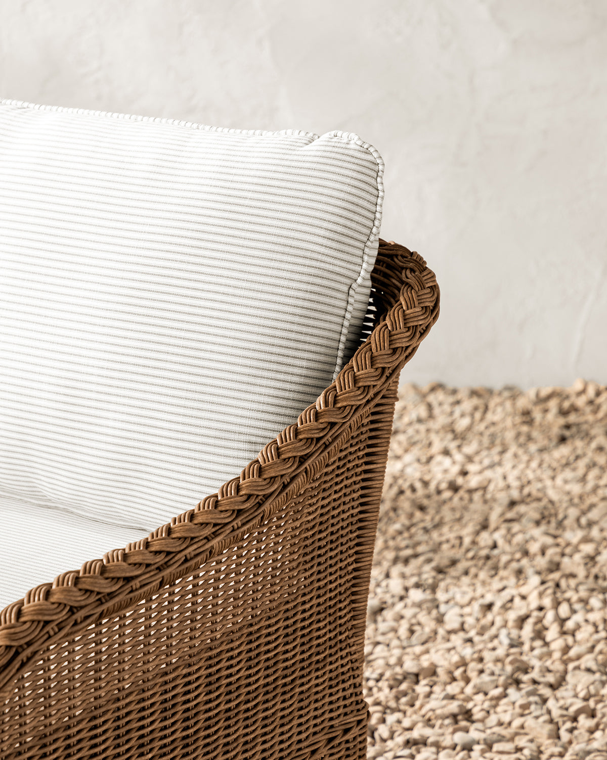 The Haviland Outdoor Swivel Lounge Chair features a wicker frame and a white striped cushion, set on a light pebble floor by an off-white textured wall—ideal as a stylish, weather-resistant outdoor chair, by Vendixs