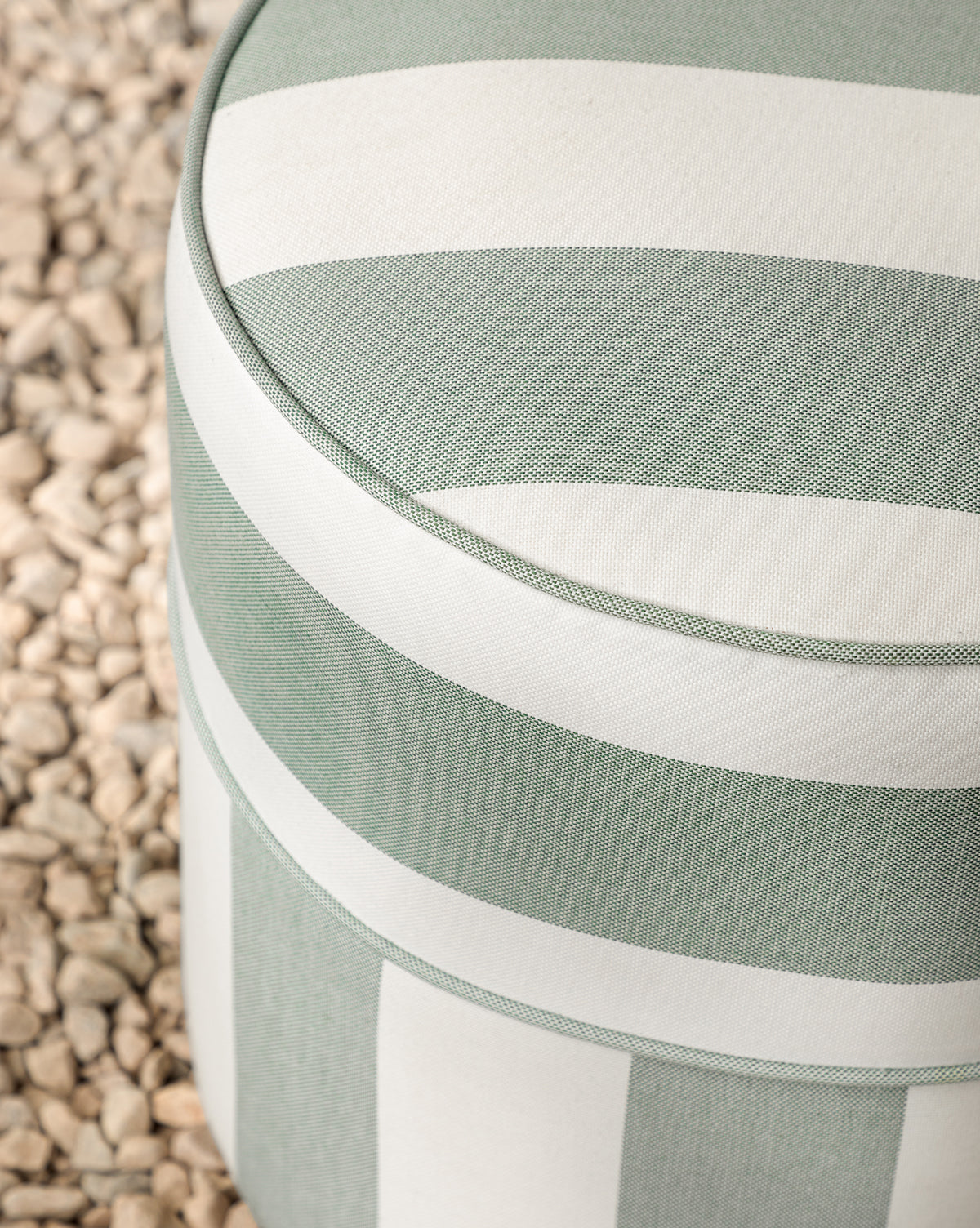 The Makerspalm Haviland Striped Ottoman features light green and white upholstery and sits on light-colored pebbles, offering a charming, weather-resistant addition to any patio or garden space. Vendixs