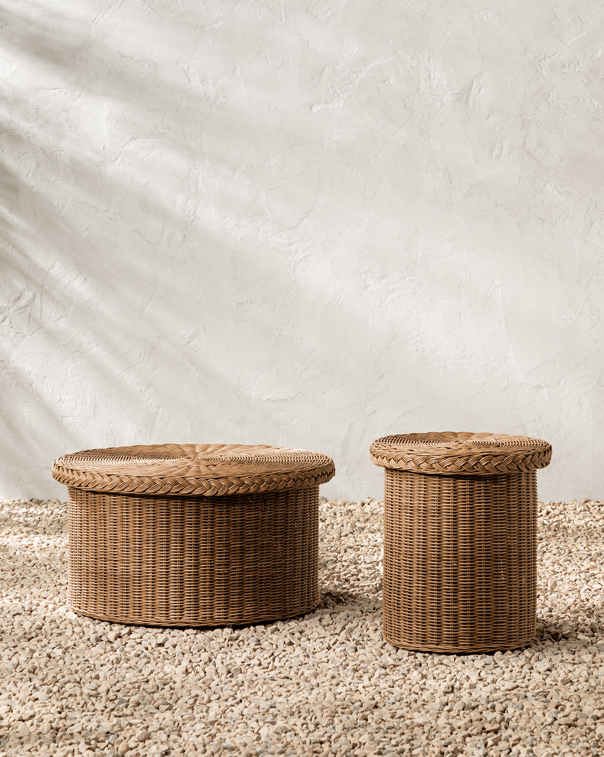 The Haviland Side Table, featuring two round wicker baskets with lids in varying sizes, sits on a pebble floor against a light stucco wall—ideal as weather-resistant accents or as a multifunctional outdoor side table, by Vendixs