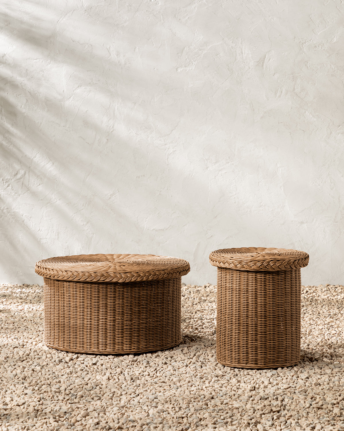 The Haviland Coffee Table, featuring two round wicker baskets with lids—one larger than the other—rests on a textured pebble floor against a light plastered wall with soft shadows, by Vendixs
