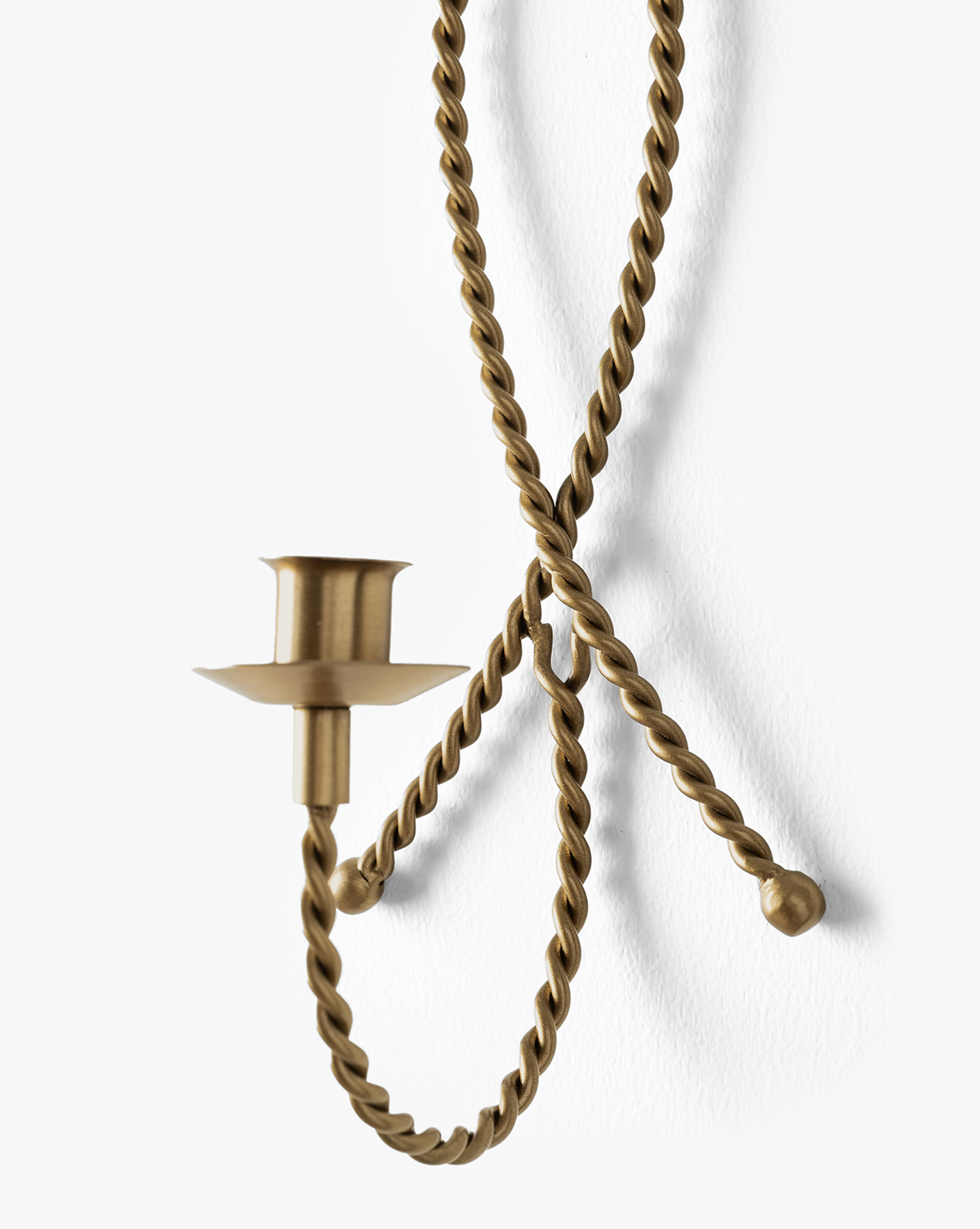 The Hearst Taper Holder is a wall-mounted, sculptural brass candle holder with a twisted, rope-like design, curled ends, and an empty candle cup, displayed against a white background, by Vendixs