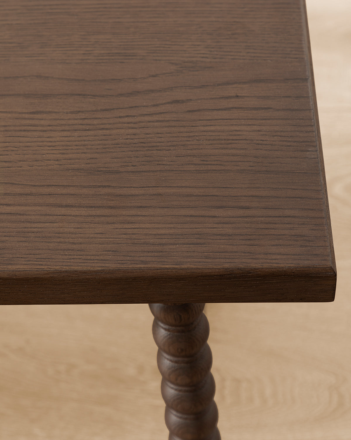 A close-up of the Heathcliff Bench highlights its dark walnut oak finish and distinct wood grain, featuring a corner of the tabletop and a decorative turned spiral leg, by Vendixs