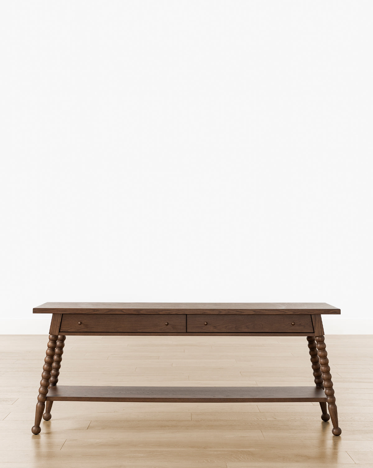 The Heathcliff Console features a dark walnut oak finish, two drawers, turned spindle legs, and a lower shelf, shown on a light wood floor against a plain white background, by McGee & Co.