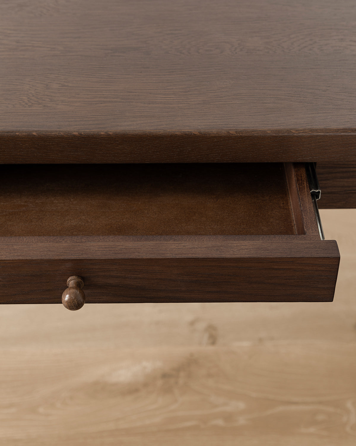 A close-up of the Heathcliff Desks partially open wooden drawer with a round knob, shown against a light wood floor background by Vendixs