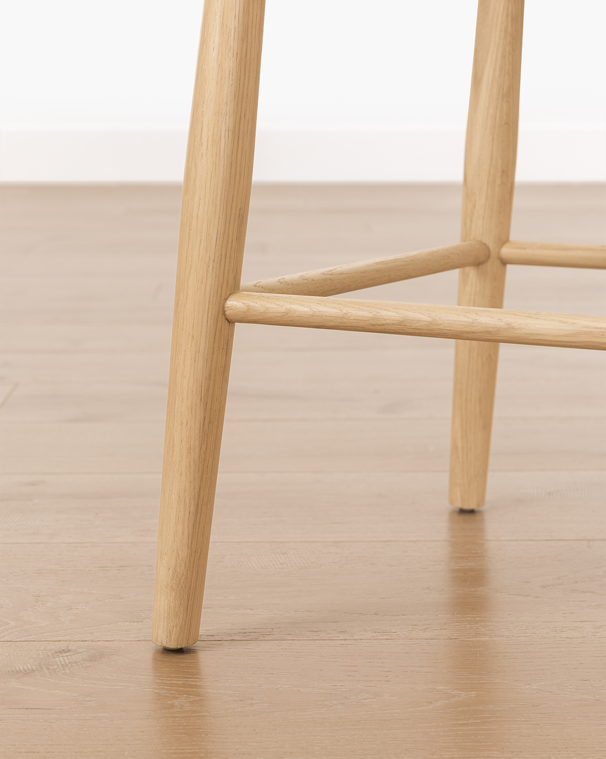 Close-up of Hemingway Chair solid wood legs on a light brown wood floor, with a white wall in the background, by Vendixs