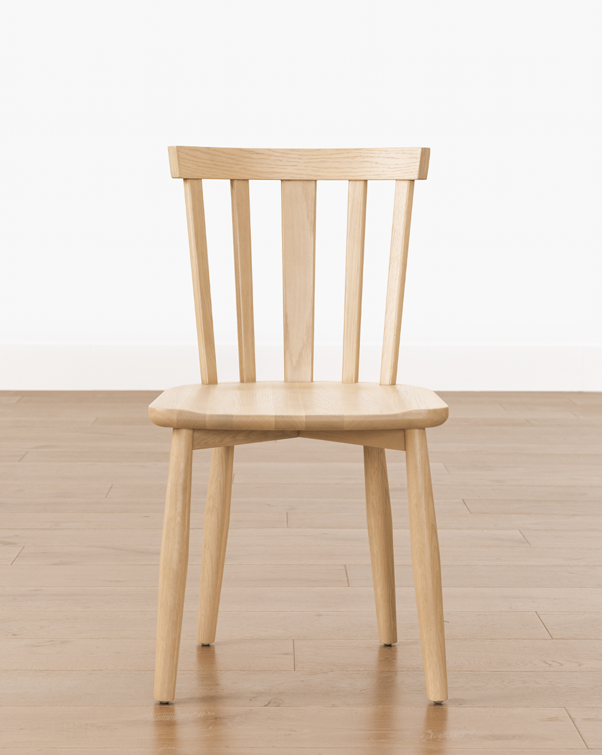 The Hemingway Chair, crafted from solid wood with a slatted backrest and four legs, is shown on a light wooden floor against a plain white wall, by Vendixs
