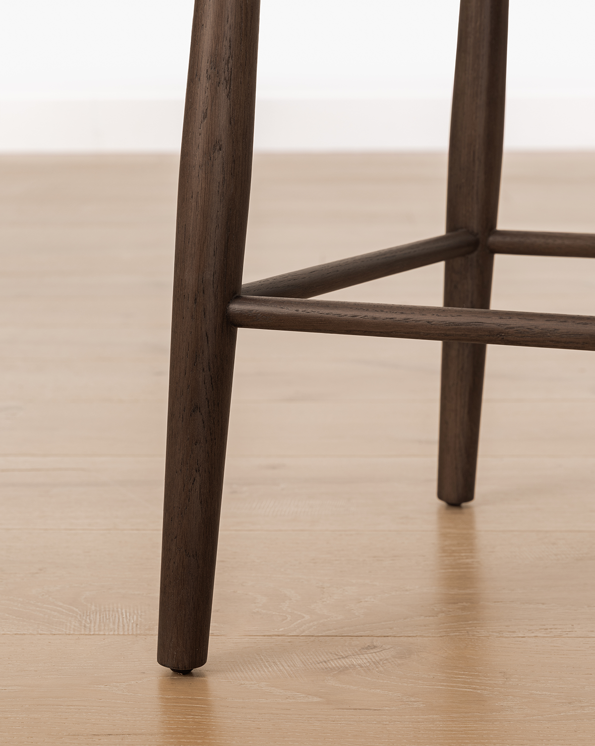 Close-up of the Hemingway Chair's wooden legs and footrest on a light wood floor, highlighting its dark brown finish and sturdy, simple design—this solid wood chair brings timeless appeal to any space, by Vendixs