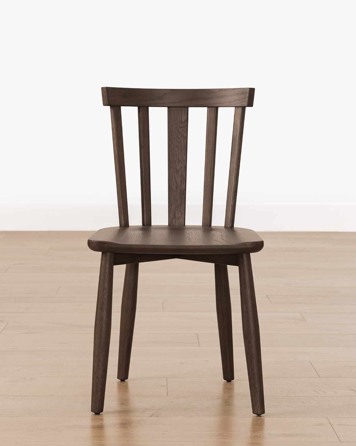 A Hemingway Chair with a dark wood finish, slatted backrest, and angled legs sits on a light wood floor against a plain white wall, by Vendixs