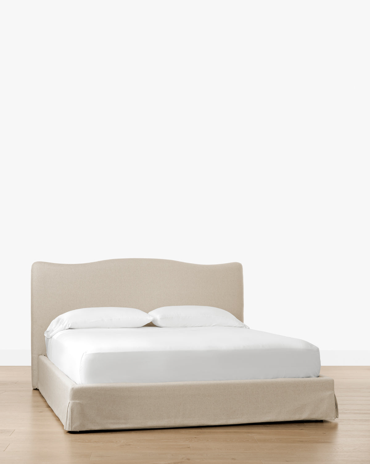 The Henrietta Bed (Ready to Ship), featuring beige upholstery and a low curved headboard, offers effortless bedroom styling with white bedding on a light wooden floor against a plain white background, by Vendixs