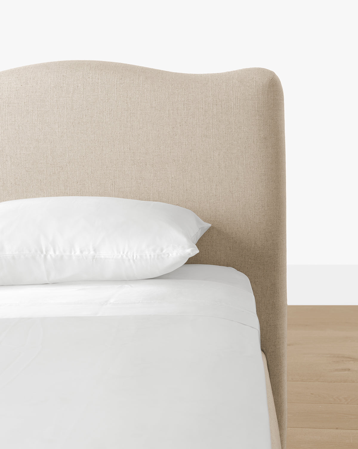 The Henrietta Bed (Ready to Ship) features a beige curved upholstered headboard, white pillow and bedding, set on a light wood floor—an elegant choice for stylish bedrooms with a clean, modern look, by Vendixs