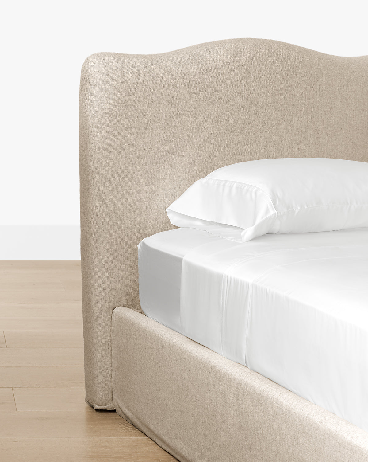 A close-up of the Henrietta Bed (Ready to Ship) showcases its beige curved upholstered headboard and frame, neatly made with white sheets and pillow on a light wood floor—ideal for elegant bedroom decor, by Vendixs
