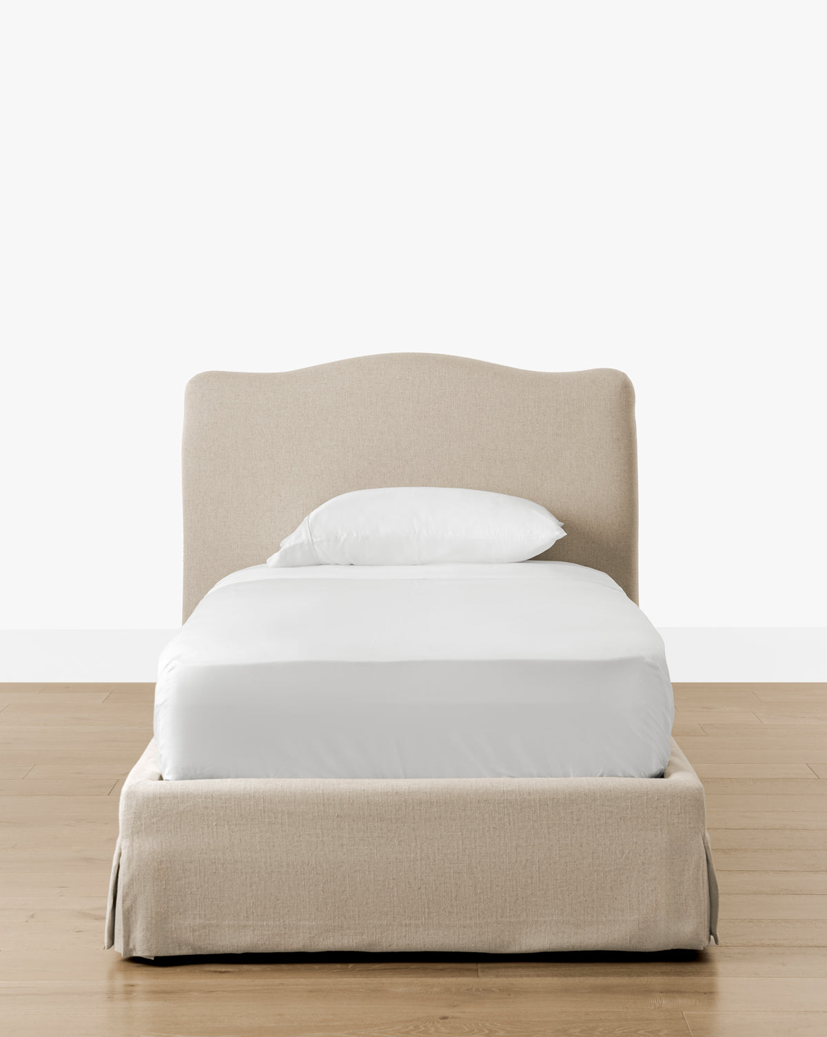 The Henrietta Bed (Ready to Ship), featuring beige upholstery and a curved headboard, is dressed in white bedding with a single pillow, set on a light wood floor against a plain white background—perfect for refined bedroom styling by Vendixs