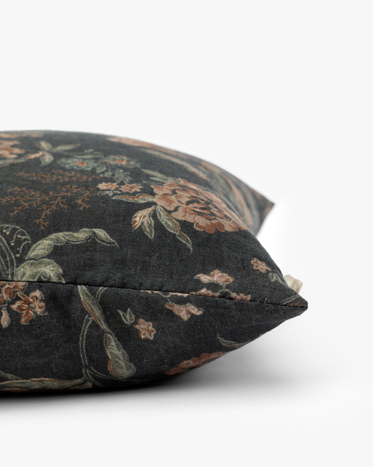 A close-up side view of the Hestercombe Pillow Cover, a vintage-inspired decorative pillow with dark fabric showcasing an intricate floral pattern in muted green and brown on a white background, by Vendixs