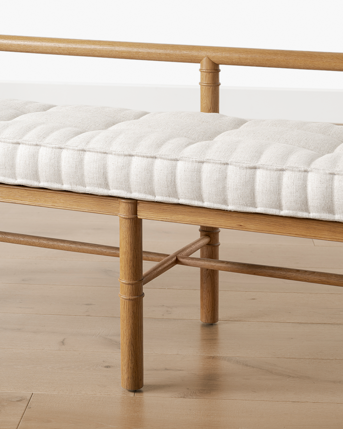 A close-up of the Hindley Bench reveals its solid wood frame, round legs, crossbar support, and a light beige tufted cushion on top, elegantly situated on a light wood floor, by Vendixs