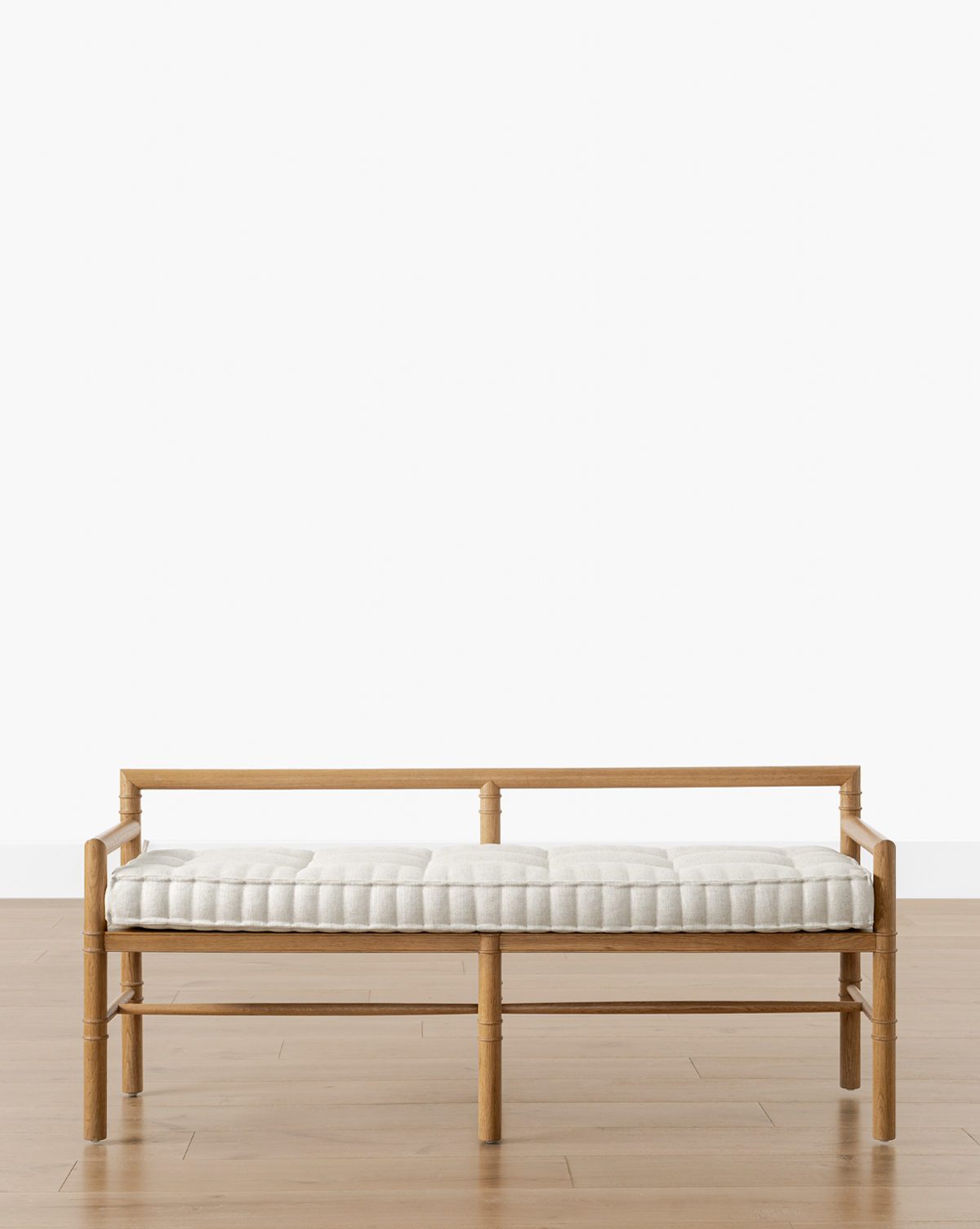 The Hindley Bench features a simple frame and light-colored tufted cushion, shown on a wooden floor against a plain white background, by Vendixs