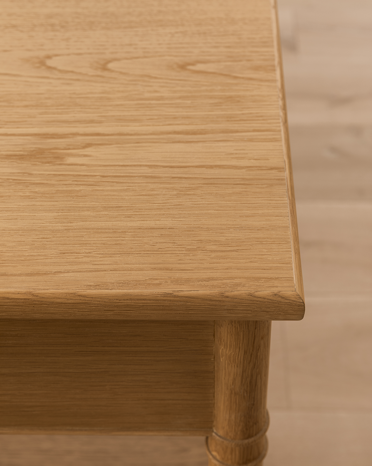 Close-up of the Hindley Console, featuring a smooth, light oak finish on the tabletop and rounded leg, set against a light wood floor background, by Vendixs