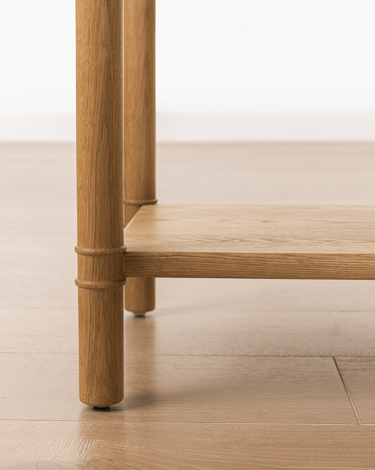 Close-up of the Hindley Console's oak leg and lower shelf on a light wood floor, showcasing its smooth finish and natural grain—perfect as a stylish entryway table, by Vendixs