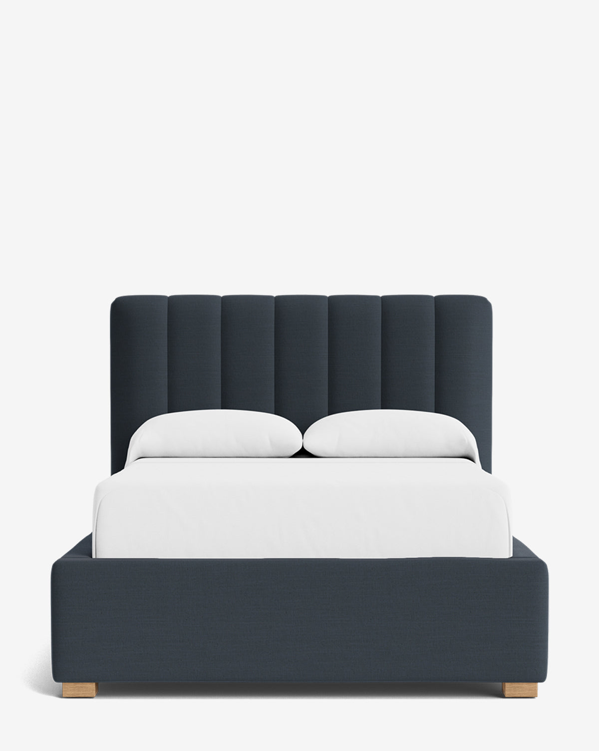 The Hoffman Bed Low Headboard features a dark blue upholstered frame and customizable vertical channel-tufted headboard, dressed in white bedding with two pillows, all set against a plain white background by McGee & Co.