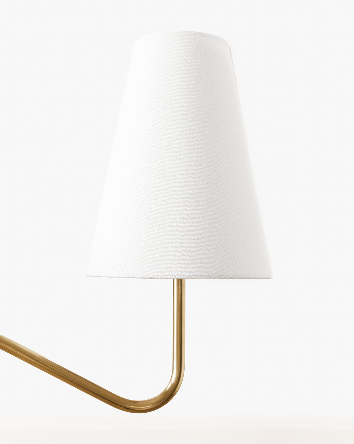 The Holloway Floor Lamp features a conical white shade and a curved antique brass arm, showcased against a plain white background, by Vendixs