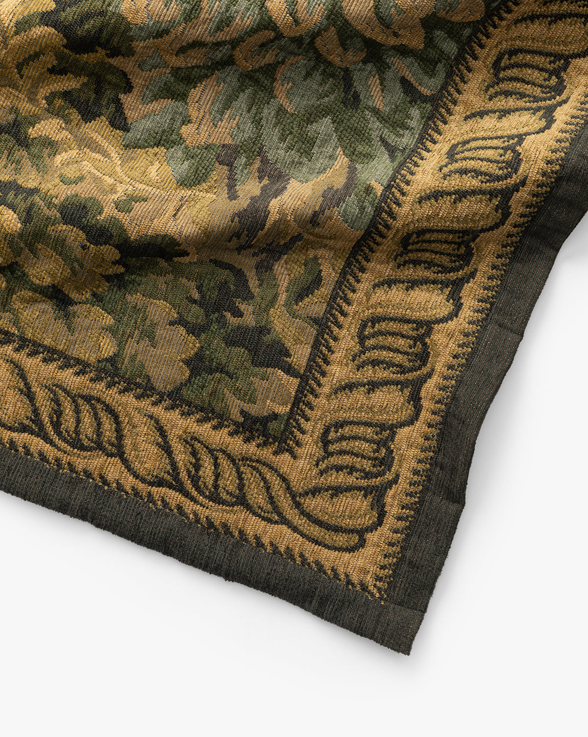 A close-up of the Hortensia Wall Tapestry shows a woven floral and leafy pattern in green, gold, and black tones with an intricate decorative border framing the textiles corner, by Vendixs