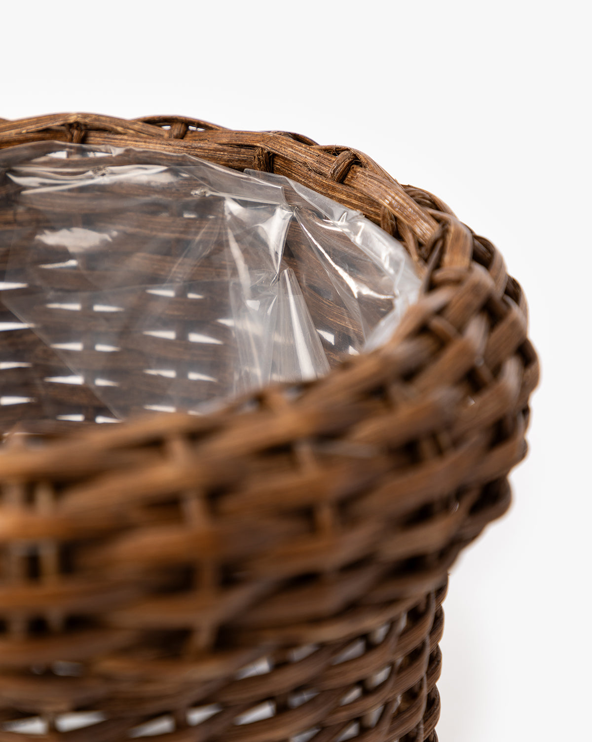 A close-up of the Huger Woven Planter, a brown woven basket featuring a clear plastic liner inside, set against a plain white background, by Vendixs
