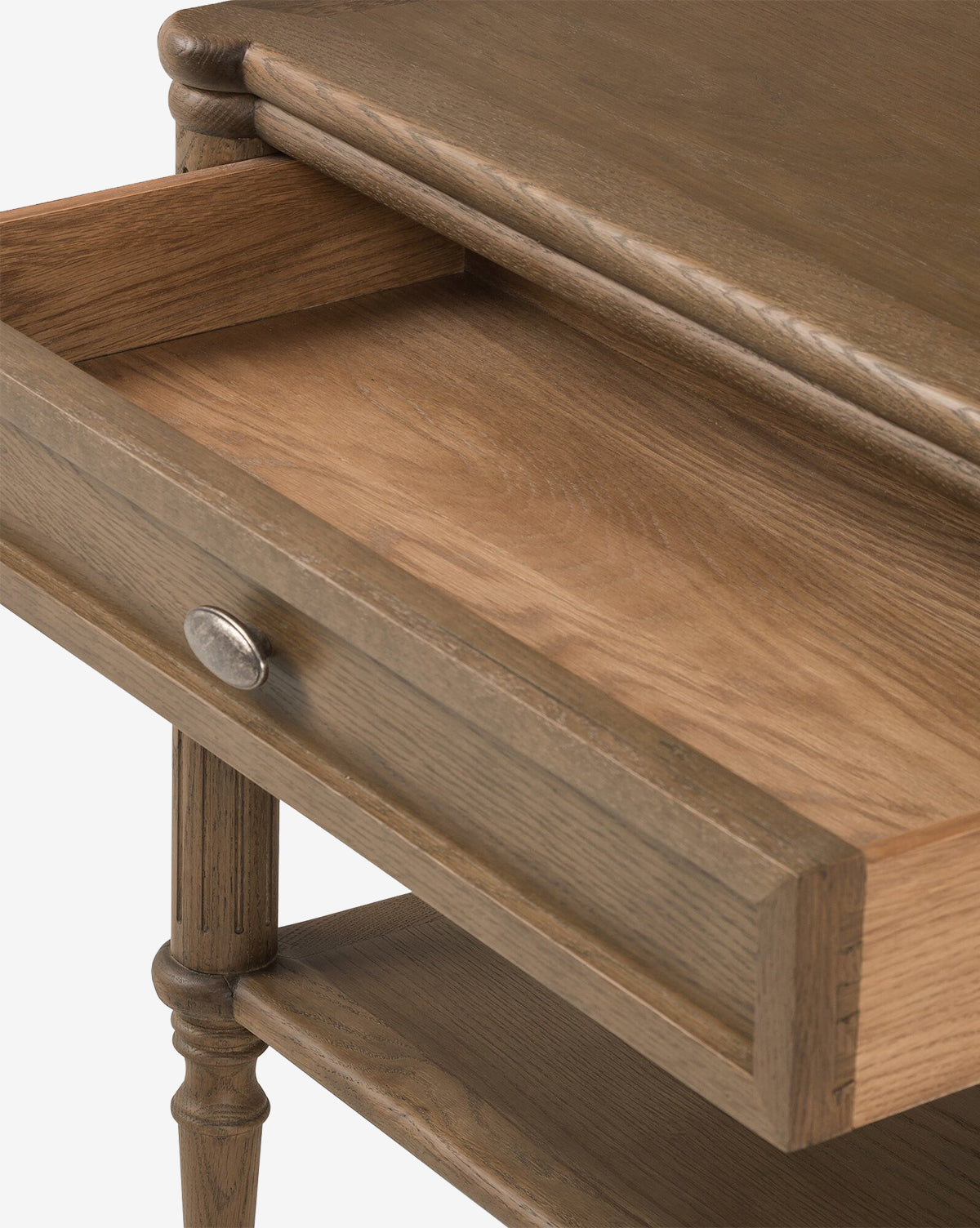 A close-up of the Humphrey Nightstand in oak shows its open drawer with a round metal knob and elegant turned legs. The natural wood finish adds charm, making this nightstand a timeless addition to any traditional bedroom décor, by Vendixs