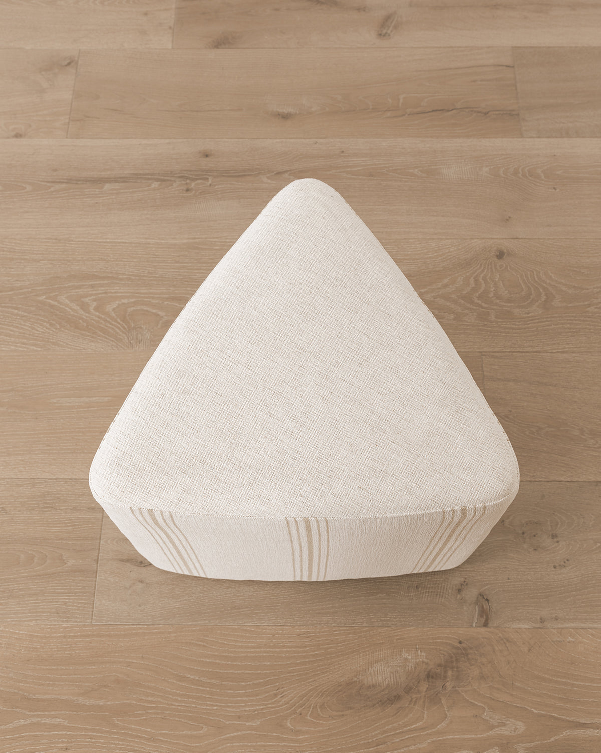 The Jacques Ottoman by Dongguan City Baby Furniture Co., Ltd features a triangular design, cream Crypton striped upholstery, and sits on a light wood floor—ideal for bringing stylish durability to kids’ rooms. Vendixs