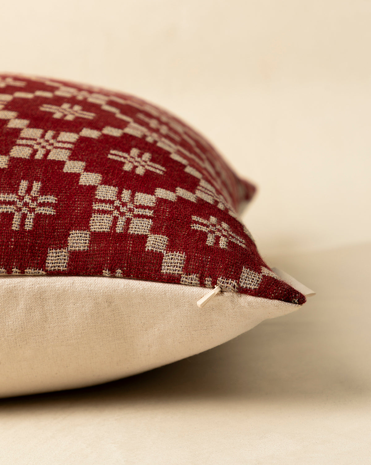 The Jude Pillow Cover features a red and beige geometric woven top, plain beige bottom, and a delicate bow at one corner—ideal for seasonal styling. Shown here on a light surface in close-up detail, by Vendixs