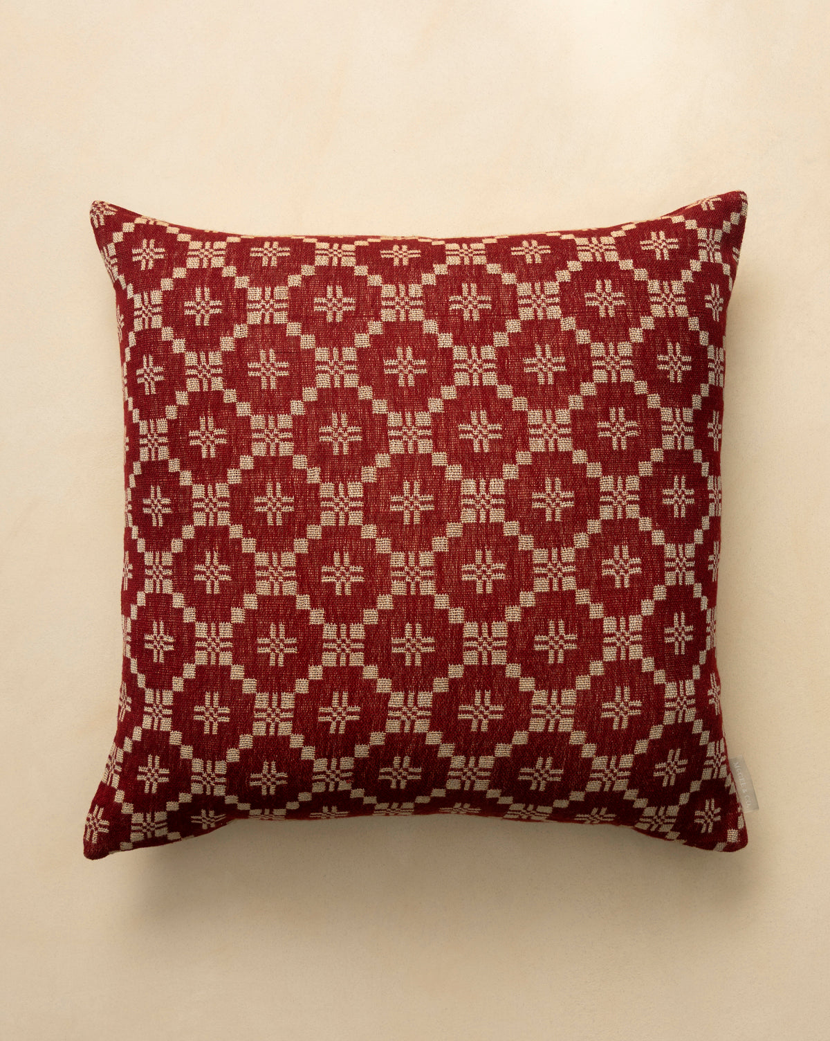 The Jude Pillow Cover is a square, dark red woven cover with a geometric beige diamond and star pattern, shown on a light beige surface, by Vendixs