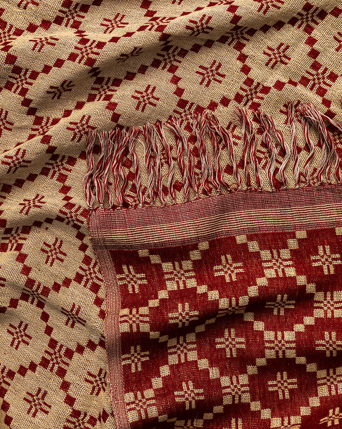 A close-up of the Jude Reversible Woven Throw, showcasing its vintage-inspired red and beige geometric pattern, fringed edges, and intricate diamond and cross designs that reflect traditional craftsmanship, by Vendixs