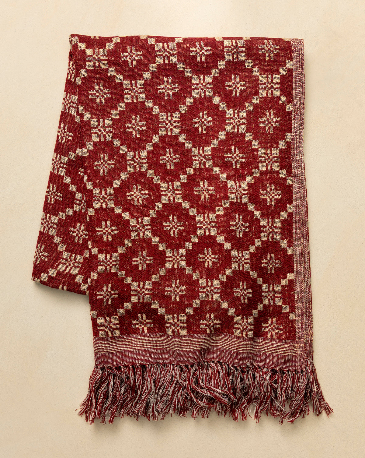 The Jude Reversible Woven Throw features a vintage-inspired red and beige geometric floral pattern with twisted fringe, making it a cozy accent for any light beige surface, by Vendixs
