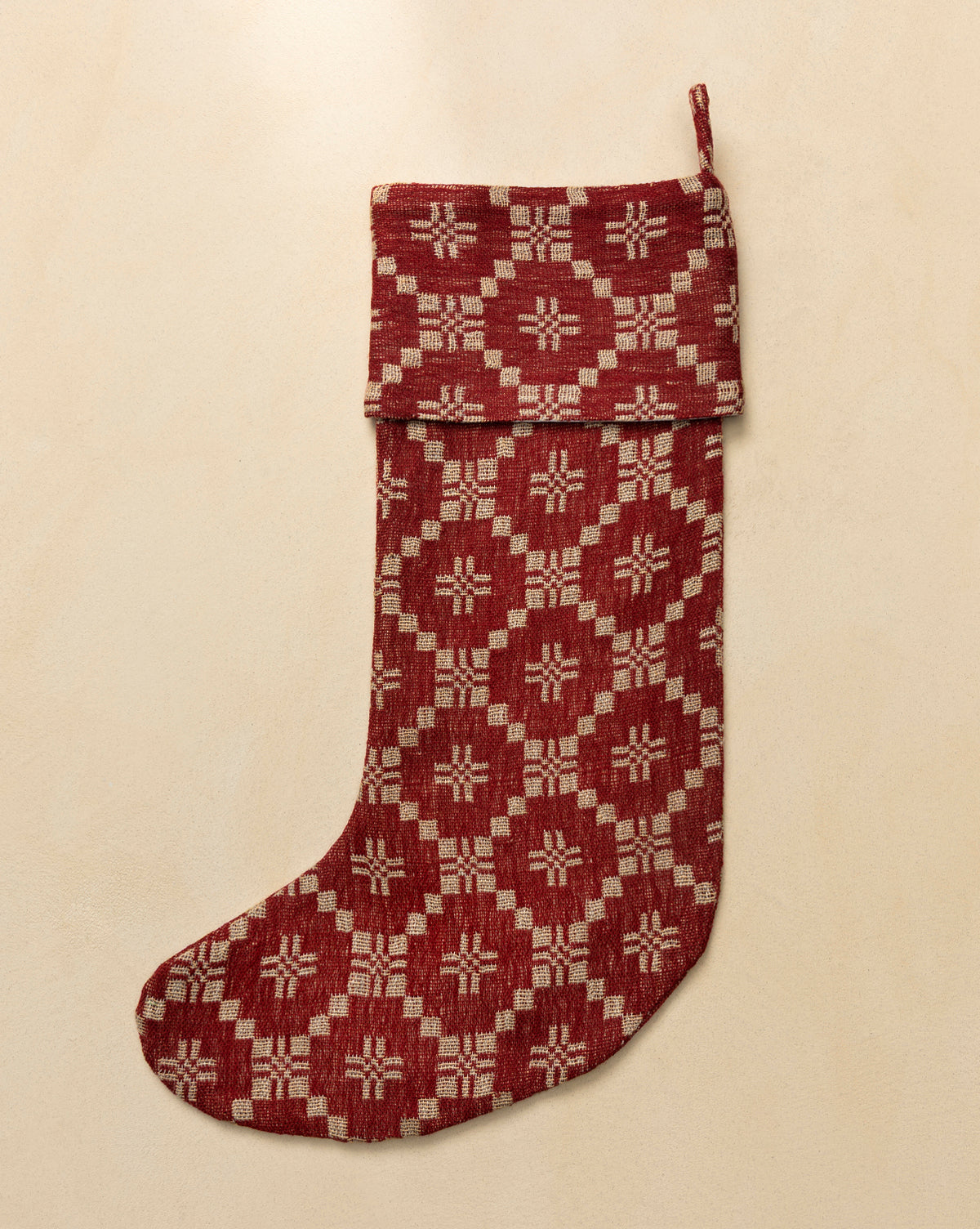 The Jude Stocking, a red and beige vintage design with a folded cuff and geometric woven pattern, features rich texture and lies flat on a light tan surface—ideal for adding charm to your holiday mantel, by Vendixs