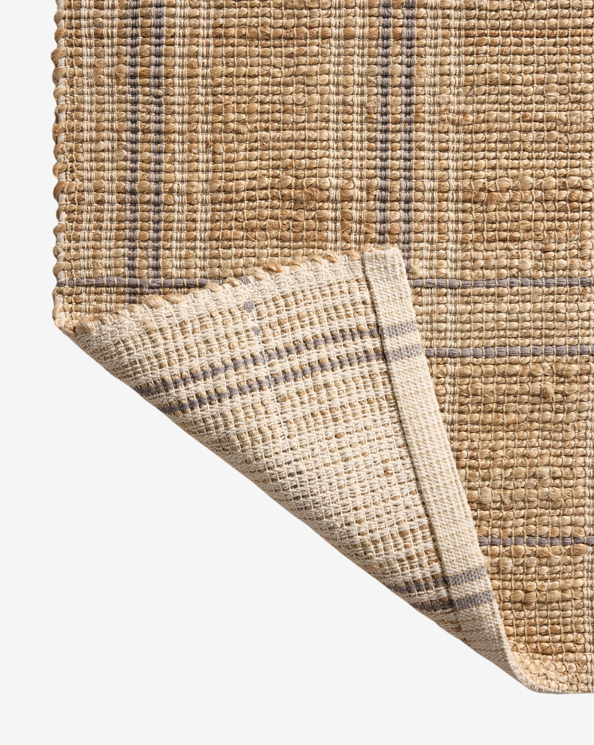 Close-up of a handwoven rug in tan and beige plaid, with one corner turned to show the pattern and natural, coarse texture—styled like the Judy Jute Rug Collection No. 2, by Vendixs