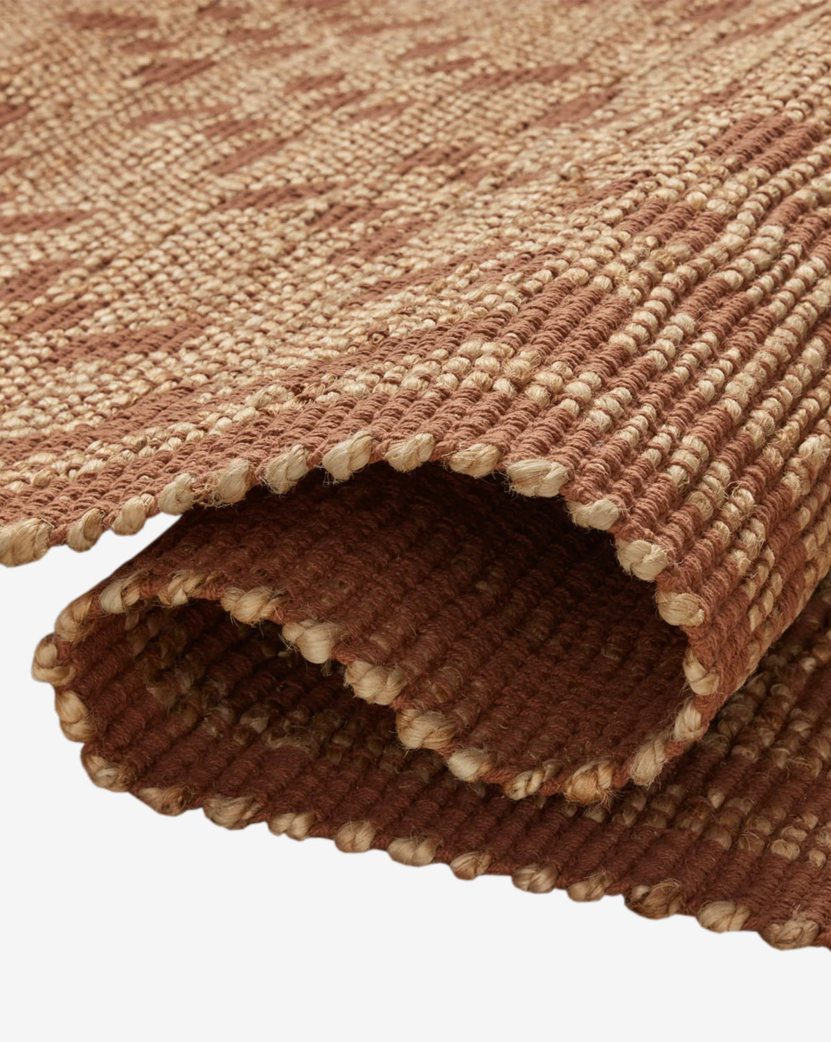 A close-up of the Judy Spice Jute Rug Collection No. 7 shows its rolled, handwoven brown and beige design with a textured surface and thick, sturdy fibers—ideal as a durable, neutral accent rug for any space, by Vendixs