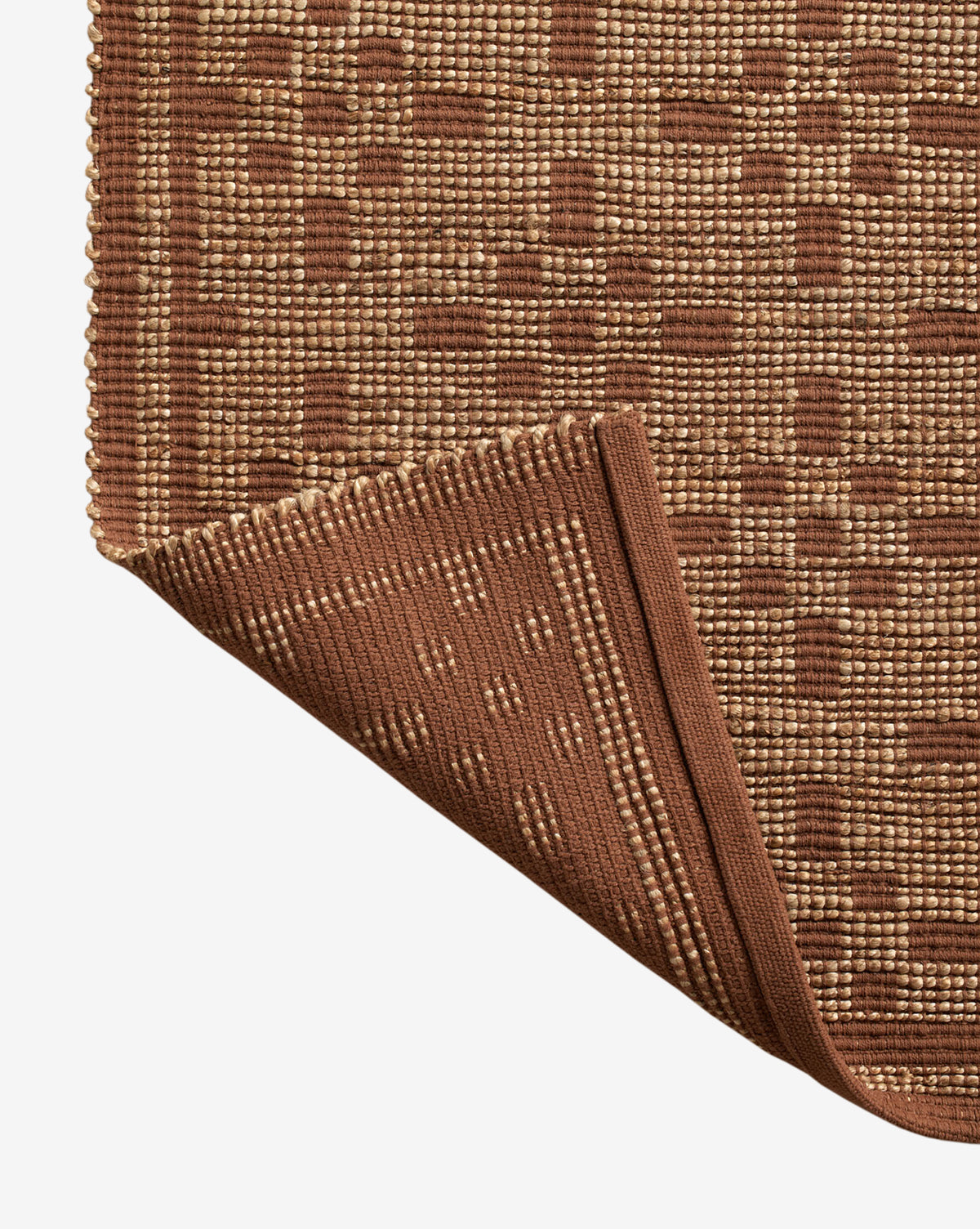 A close-up of the Judy Spice Jute Rug Collection No. 7 showcases its handwoven geometric square pattern, with one corner folded to display the underside and neatly finished edge, by Vendixs