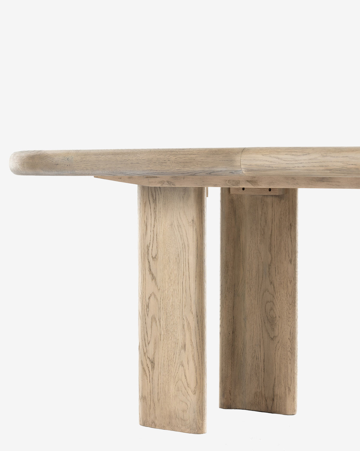 A close-up side view of the Juliana Extension Dining Table, featuring a thick, rounded solid oak top and two wide rectangular legs, highlighting its light natural wood grain and modern design against a plain white background, by McGee & Co.
